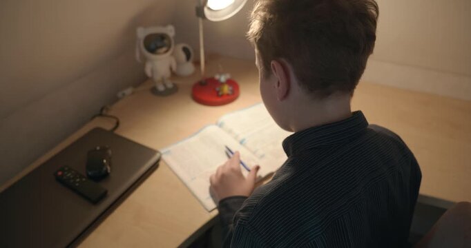 Kid Boy Doing Homework in Workbook Writing with Pen on Table Desk. 4K 10-bit
