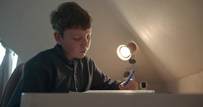 Kid Boy Doing Homework in Workbook Writing with Pen on Table Desk. 4K 10-bit