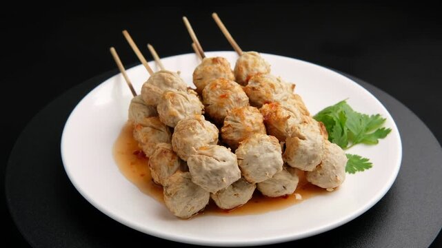 Charcoal grilled Thai Pork meatballs on skewers on white plate with chilli sauce.