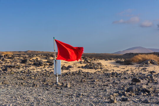 Red warning flag blowing in wind across barren volcanic desert landscape background