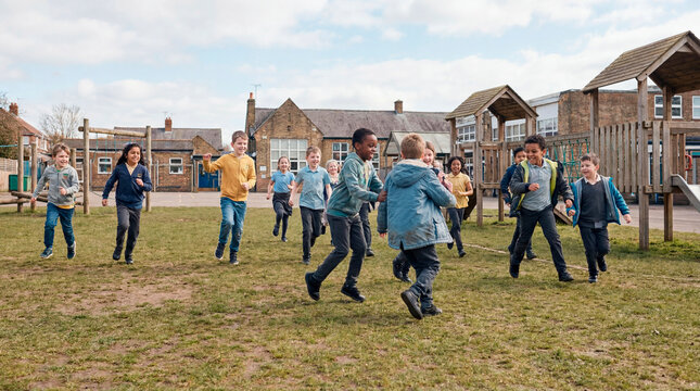 Energetic diverse children running and playing on grassy school playground at recess