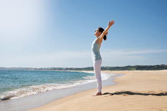 woman standing on a sandy beach with arms raised toward the sun