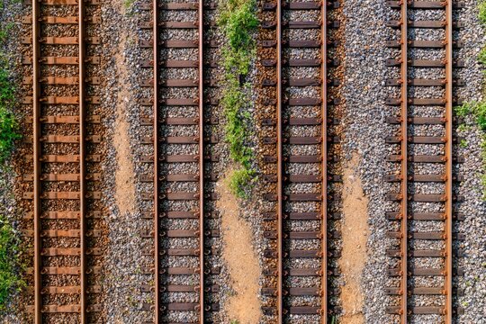 Overhead view of multiple parallel rusty train tracks, gravel, and weeds