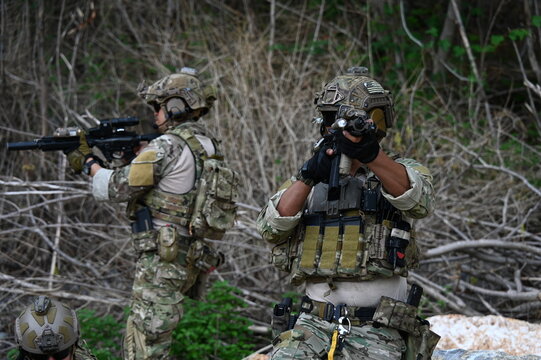 Tactical operator in camouflage gear rests with a rifle on rocky terrain during outdoor field training. Concept of military exercise, security, readiness, and tactical operations.