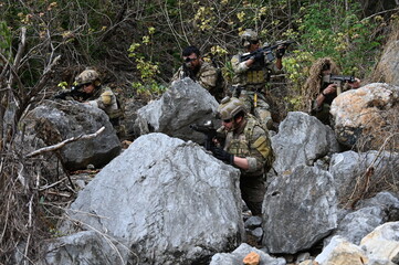Obraz premium Dedicated squad of professional armed military soldiers walking in patrol formation along a rugged rocky mountain cliff during a dangerous tactical combat mission or outdoor training exercise.
