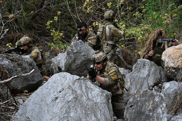 Obraz premium Dedicated squad of professional armed military soldiers walking in patrol formation along a rugged rocky mountain cliff during a dangerous tactical combat mission or outdoor training exercise.