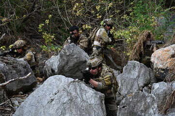 Obraz premium Dedicated squad of professional armed military soldiers walking in patrol formation along a rugged rocky mountain cliff during a dangerous tactical combat mission or outdoor training exercise.