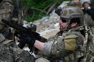 Obraz premium Focused military infantry soldier lying prone on rugged rocky terrain aiming a tactical assault rifle during a dangerous combat training mission for national defense and special security.