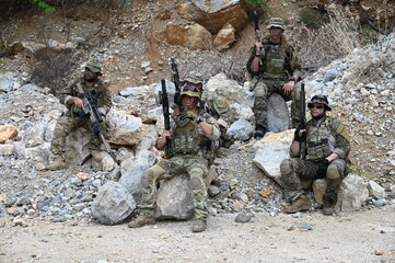 Obraz premium Dedicated squad of professional armed military soldiers walking in patrol formation along a rugged rocky mountain cliff during a dangerous tactical combat mission or outdoor training exercise.