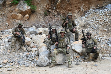 Obraz premium Dedicated squad of professional armed military soldiers walking in patrol formation along a rugged rocky mountain cliff during a dangerous tactical combat mission or outdoor training exercise.