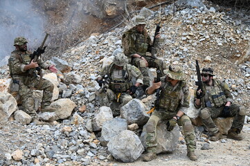 Obraz premium Dedicated squad of professional armed military soldiers walking in patrol formation along a rugged rocky mountain cliff during a dangerous tactical combat mission or outdoor training exercise.