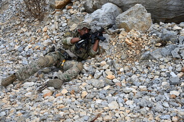 Obraz premium Focused military infantry soldier lying prone on rugged rocky terrain aiming a tactical assault rifle during a dangerous combat training mission for national defense and special security.
