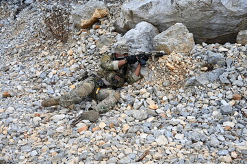 Obraz premium Focused military infantry soldier lying prone on rugged rocky terrain aiming a tactical assault rifle during a dangerous combat training mission for national defense and special security.