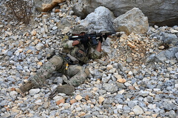 Obraz premium Focused military infantry soldier lying prone on rugged rocky terrain aiming a tactical assault rifle during a dangerous combat training mission for national defense and special security.