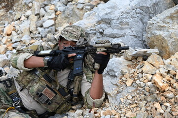 Obraz premium Focused military infantry soldier lying prone on rugged rocky terrain aiming a tactical assault rifle during a dangerous combat training mission for national defense and special security.