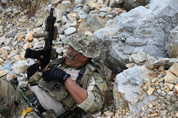 Obraz premium Focused military infantry soldier lying prone on rugged rocky terrain aiming a tactical assault rifle during a dangerous combat training mission for national defense and special security.