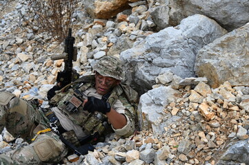 Obraz premium Focused military infantry soldier lying prone on rugged rocky terrain aiming a tactical assault rifle during a dangerous combat training mission for national defense and special security.