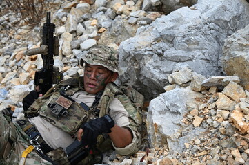 Obraz premium Focused military infantry soldier lying prone on rugged rocky terrain aiming a tactical assault rifle during a dangerous combat training mission for national defense and special security.