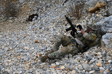 Obraz premium Focused military infantry soldier lying prone on rugged rocky terrain aiming a tactical assault rifle during a dangerous combat training mission for national defense and special security.