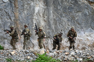 Obraz premium Dedicated squad of professional armed military soldiers walking in patrol formation along a rugged rocky mountain cliff during a dangerous tactical combat mission or outdoor training exercise.