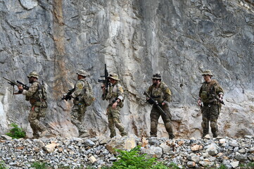 Obraz premium Dedicated squad of professional armed military soldiers walking in patrol formation along a rugged rocky mountain cliff during a dangerous tactical combat mission or outdoor training exercise.