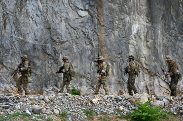 Obraz premium Dedicated squad of professional armed military soldiers walking in patrol formation along a rugged rocky mountain cliff during a dangerous tactical combat mission or outdoor training exercise.