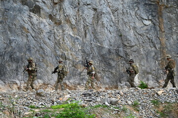 Obraz premium Dedicated squad of professional armed military soldiers walking in patrol formation along a rugged rocky mountain cliff during a dangerous tactical combat mission or outdoor training exercise.