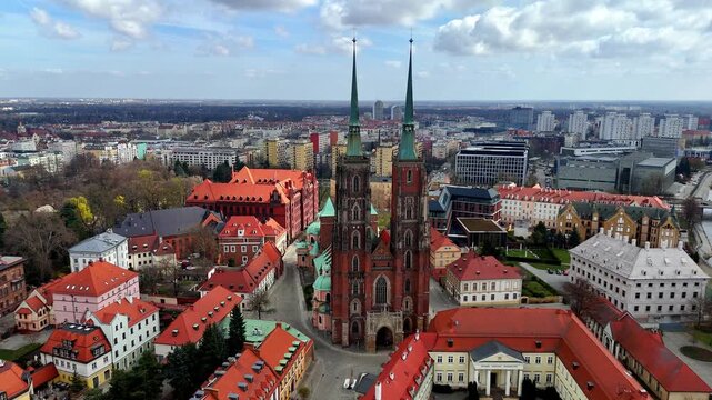 Panoramic aerial view of Ostrow Tumski in Wroclaw, featuring the monumental Cathedral of St. John the Baptist, historic buildings with red roofs, surrounding greenery, and the modern city skyline in t