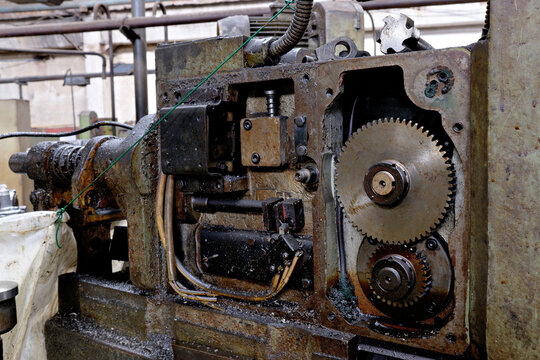 Close up shot of an open gearbox mechanism displaying steel spur gears, oil, and wiring inside heavy industrial manufacturing machinery.