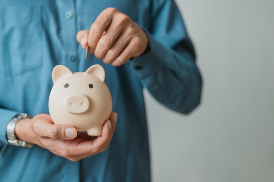 Person inserting a coin into a piggy bank to represent saving money, personal finance, budgeting, and long-term wealth growth.