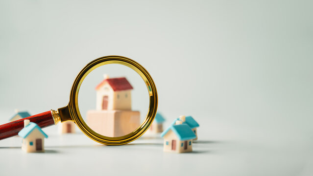 Magnifying glass examining miniature houses represents property management, real estate analysis, and investment opportunities.