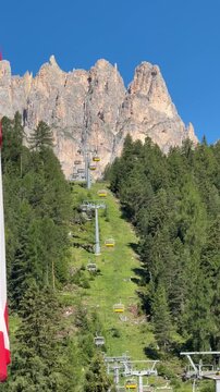 Chairlift ascending through alpine forest beneath Rosengarten peaks, Italy