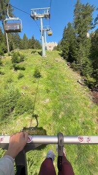 First-person perspective from a chairlift ascending through alpine forest toward the spectacular Rosengarten (Catinaccio) massif in the Dolomites, Italy