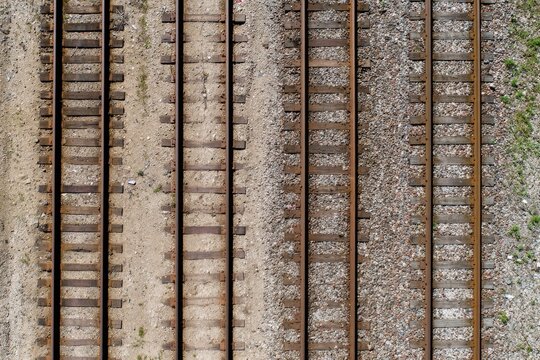 An overhead view of multiple weathered train tracks laid on gravel and earth