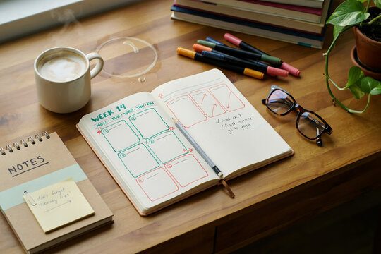 Handwritten weekly planner on wooden desk, creative bullet journal with colorful markers and coffee, cozy workspace for productivity and organization
