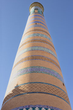 Islam Khoja minaret in Khiva viewed from below against a clear blue sky. Decorative bands of glazed tilework and brick create geometric patterns on the tapered tower. Ideal for travel publications.