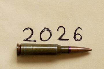 Fototapeta premium A bullet cartridge against the date 2026 written in pen on paper, on the theme of war, armed conflict, weapons