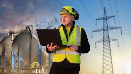 Energy industry. Power plant engineer uses laptop near storage tanks and high voltage transmission lines during site inspection © Grispb