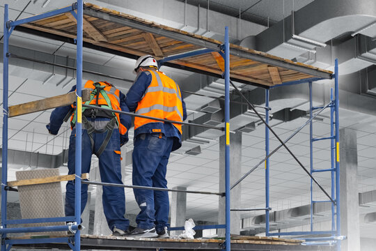 Construction, Building renovation. Two workers install ceiling ventilation and ductwork from scaffolding inside an unfinished commercial space