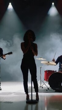 Vertical video: Spotlights starting, lead singer in dark outfit singing onstage with mic, red drums