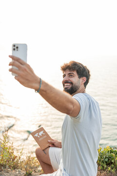 vertical Adventurous man taking selfie with smartphone by the ocean