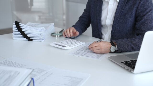 Accountant calculating tax, reviewing financial report, and managing business paperwork on a modern office desk, processing data for audit and budget planning. Audit and taxes