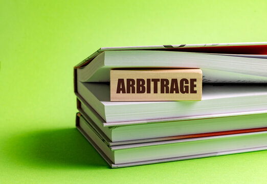 Arbitrage concept on wooden block placed on stacked books with green background representing finance trading investment
