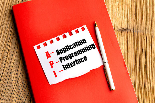 Application programming interface api acronym on torn paper with red notebook and pen on wooden desk technology concept