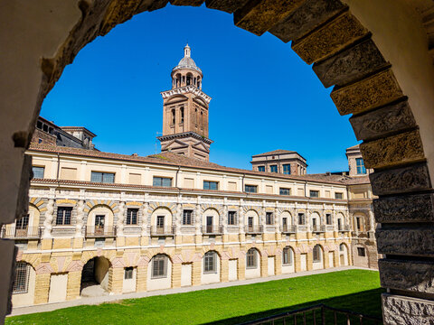 Palazzo Ducale showcasing its historic Renaissance architecture and large bell tower, viewed through an ancient stone arch framing the central courtyard lawn on a clear day
