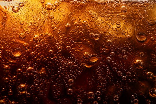 Carbonated beverage bubbles rising in amber liquid closeup