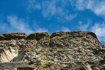 Fototapeta premium Upward View of Mossy Limestone Cliff Wall Under Blue Sky