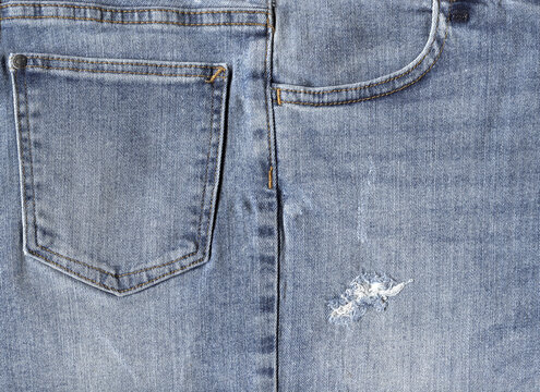 Light blue jeans cloth texture background with front and back pockets. Ripped ripped denim material close-up.