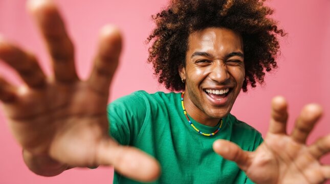 Joyful African American man with curly hair wearing a green shirt dancing against a pink background.