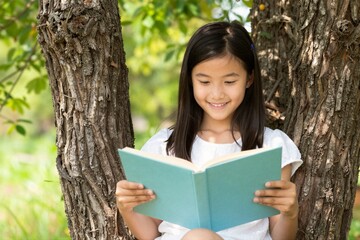 Fototapeta premium Young girl reading book while sitting between tree trunks